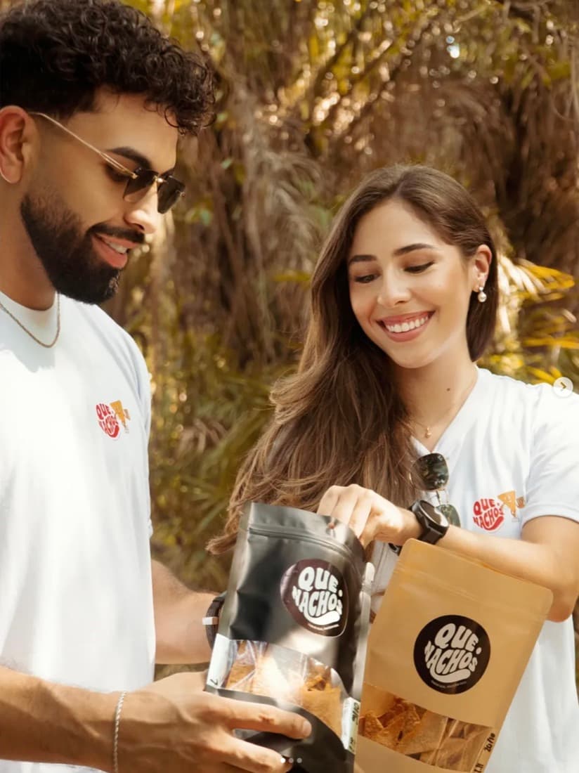 Pareja abriendo bolsas de Que Nachos negra y kraft